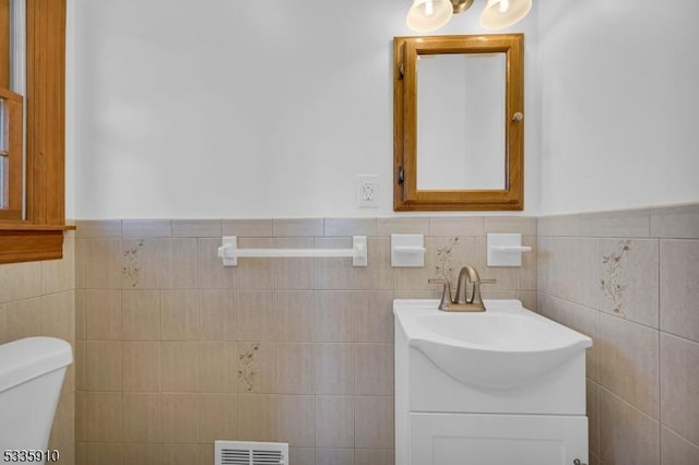 bathroom featuring vanity, toilet, and tile walls