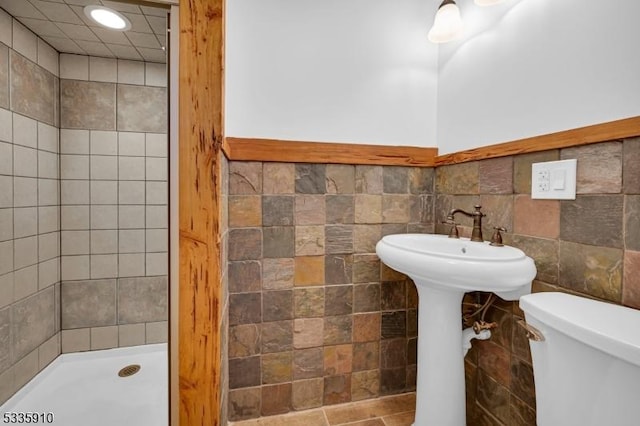 bathroom featuring a tile shower, tile walls, and toilet