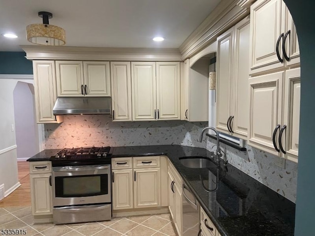 kitchen with sink, decorative backsplash, dark stone counters, light tile patterned floors, and stainless steel appliances