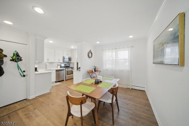 dining room featuring a baseboard heating unit, light wood finished floors, baseboards, and crown molding