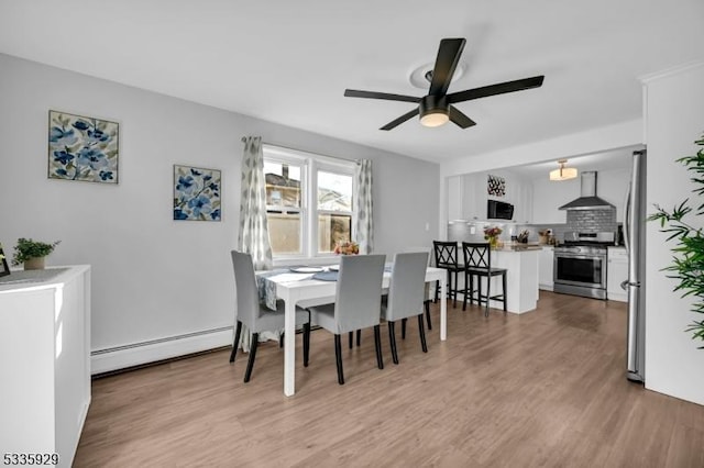 dining area featuring a baseboard heating unit, ceiling fan, and light wood-type flooring