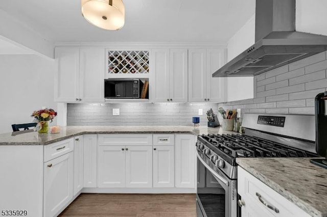 kitchen featuring stainless steel gas range oven, white cabinets, light stone counters, and range hood