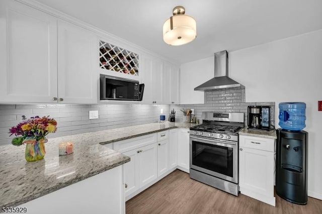 kitchen with wall chimney exhaust hood, gas stove, white cabinetry, light stone counters, and black microwave