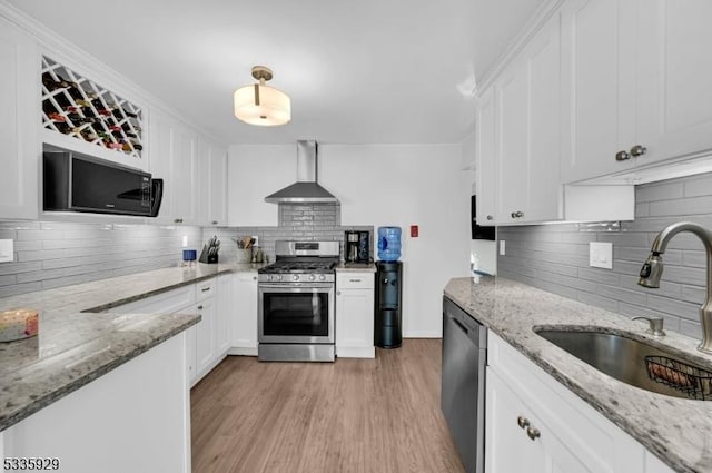 kitchen with wall chimney exhaust hood, sink, white cabinetry, light stone counters, and appliances with stainless steel finishes