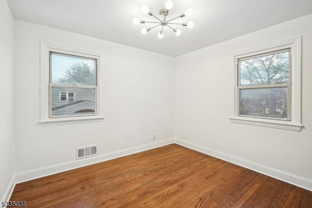 empty room with hardwood / wood-style floors and an inviting chandelier