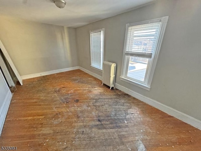 empty room featuring radiator heating unit, baseboards, and wood-type flooring