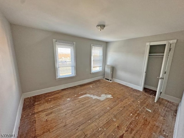 unfurnished bedroom featuring baseboards, hardwood / wood-style floors, a closet, and radiator