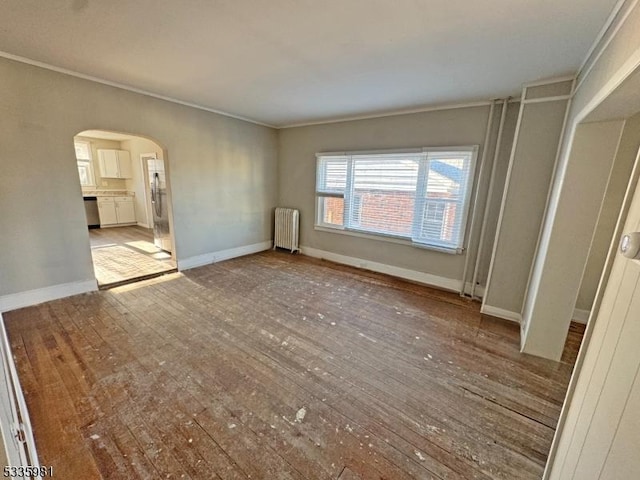 interior space featuring arched walkways, baseboards, ornamental molding, radiator, and hardwood / wood-style floors