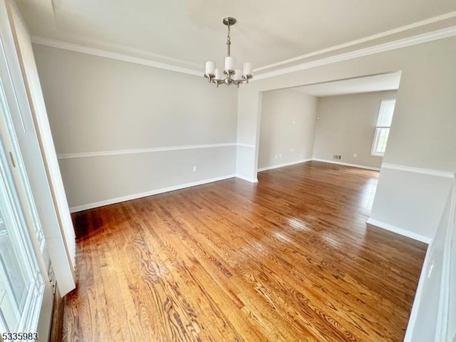 empty room featuring a notable chandelier, wood-type flooring, and ornamental molding