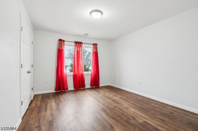 spare room with dark wood-type flooring and baseboards