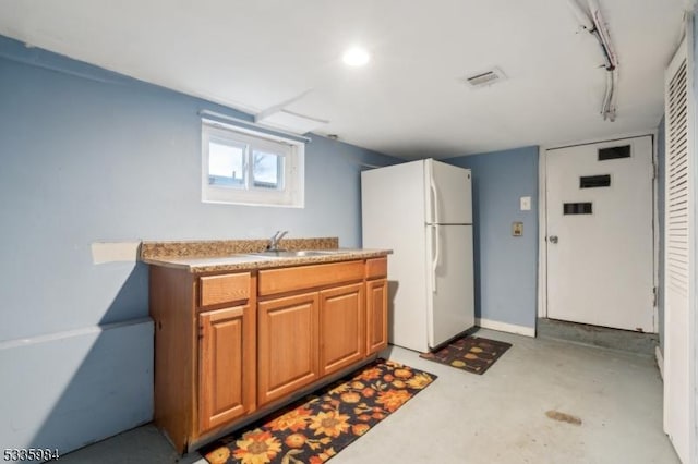 kitchen featuring concrete flooring, a sink, visible vents, freestanding refrigerator, and brown cabinetry