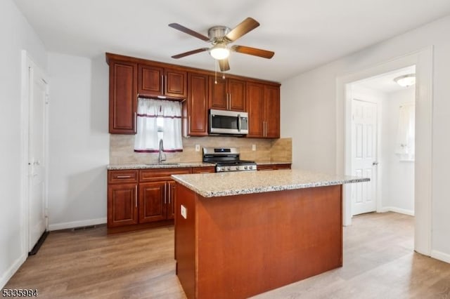 kitchen with light wood-style flooring, a kitchen island, a sink, appliances with stainless steel finishes, and tasteful backsplash