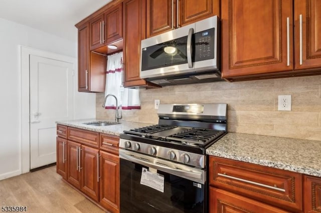 kitchen with stainless steel appliances, tasteful backsplash, a sink, and light stone countertops