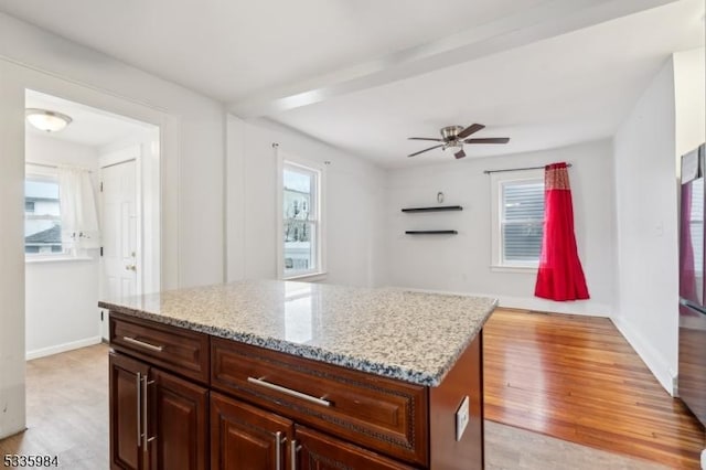 kitchen with baseboards, a kitchen island, light wood-style flooring, and light stone countertops