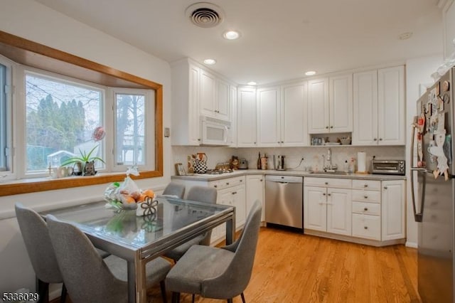 kitchen featuring light wood finished floors, stainless steel appliances, visible vents, white cabinets, and a sink