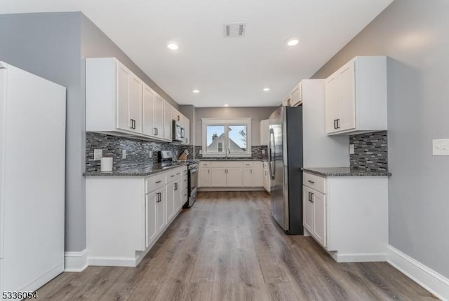 kitchen with stainless steel appliances, white cabinetry, sink, and dark stone counters