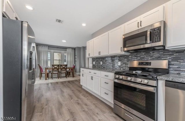 kitchen featuring light stone counters, decorative backsplash, stainless steel appliances, and white cabinets