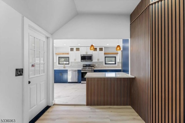 kitchen with pendant lighting, appliances with stainless steel finishes, white cabinetry, backsplash, and vaulted ceiling