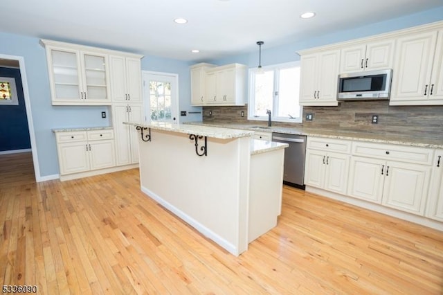 kitchen with pendant lighting, stainless steel appliances, light stone counters, white cabinets, and a kitchen island