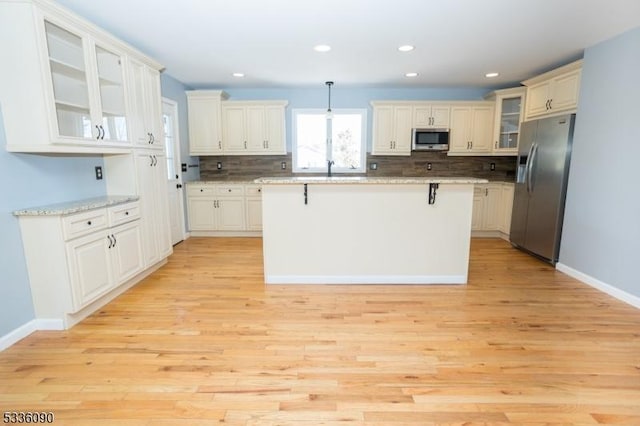 kitchen with pendant lighting, stainless steel appliances, a kitchen breakfast bar, light stone countertops, and a kitchen island