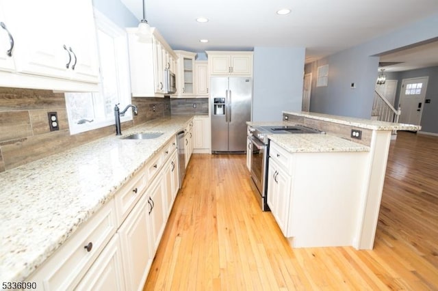 kitchen featuring pendant lighting, light hardwood / wood-style flooring, white cabinetry, stainless steel appliances, and light stone counters