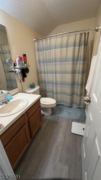 full bathroom featuring shower / bath combo, hardwood / wood-style floors, vanity, a textured ceiling, and toilet