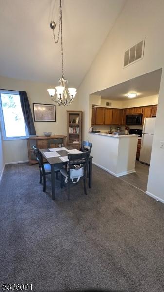 carpeted dining room featuring high vaulted ceiling and a chandelier