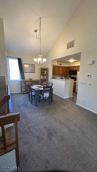 dining space featuring an inviting chandelier, high vaulted ceiling, and dark carpet