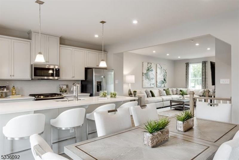 kitchen featuring sink, a breakfast bar area, hanging light fixtures, appliances with stainless steel finishes, and white cabinets