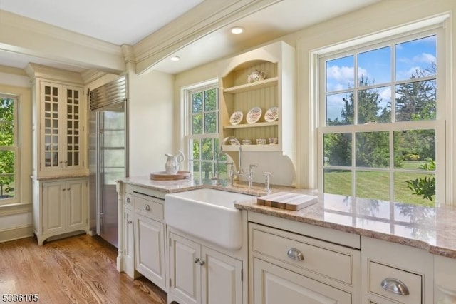 bar featuring sink, light hardwood / wood-style flooring, ornamental molding, built in fridge, and light stone countertops