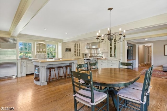 dining room with beam ceiling, ornamental molding, an inviting chandelier, and light wood-type flooring