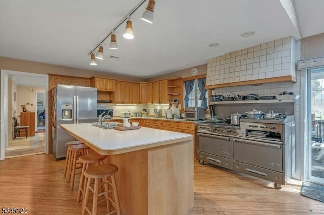 kitchen with tasteful backsplash, stainless steel fridge with ice dispenser, a kitchen island with sink, and light wood-type flooring