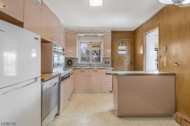 kitchen with appliances with stainless steel finishes, sink, light brown cabinetry, and wooden walls