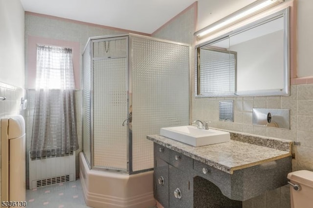 full bathroom featuring enclosed tub / shower combo, tile walls, radiator heating unit, vanity, and toilet