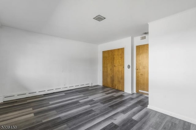 spare room featuring a baseboard heating unit and dark hardwood / wood-style floors