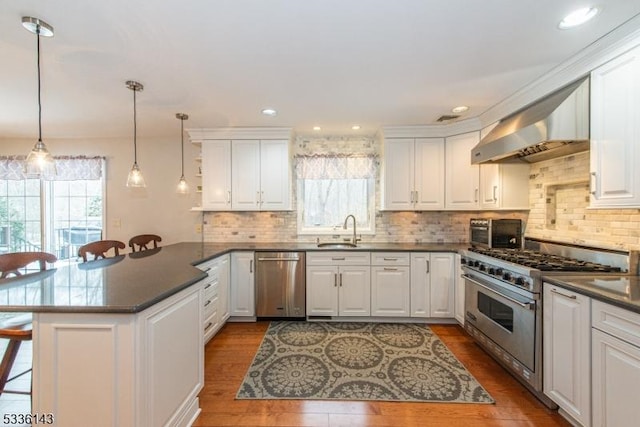 kitchen featuring sink, a breakfast bar area, appliances with stainless steel finishes, wall chimney range hood, and white cabinets