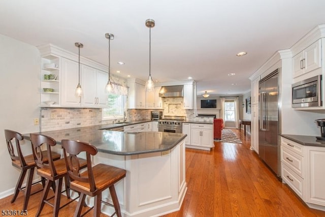 kitchen with sink, a breakfast bar area, built in appliances, kitchen peninsula, and white cabinets