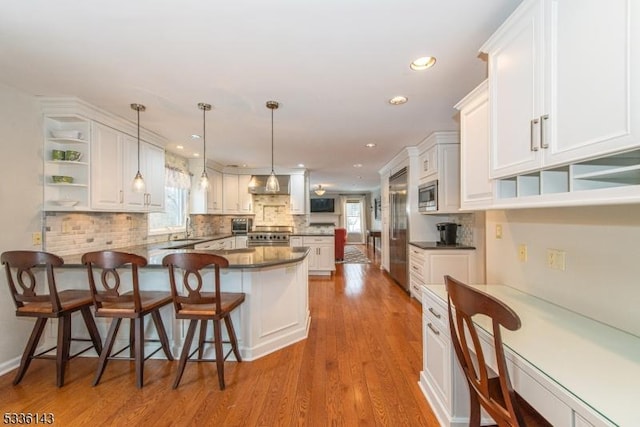 kitchen featuring a breakfast bar area, white cabinetry, built in appliances, kitchen peninsula, and a healthy amount of sunlight