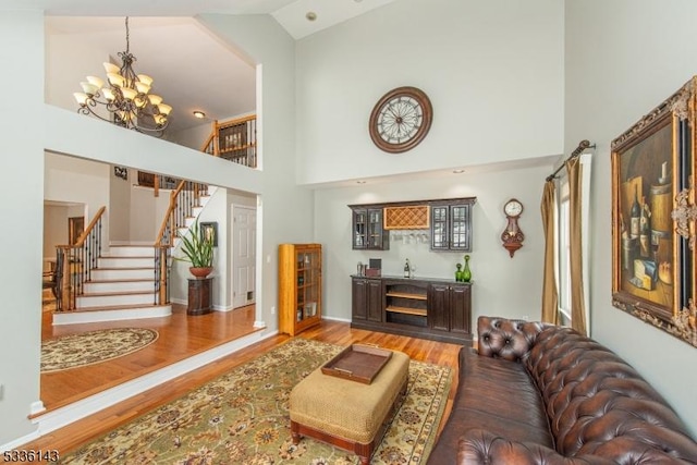 living room with a notable chandelier, wood-type flooring, high vaulted ceiling, and bar area