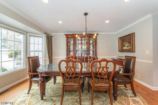 dining room with a notable chandelier, ornamental molding, and light wood-type flooring