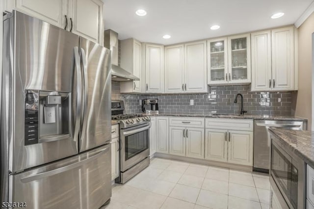 kitchen featuring stainless steel appliances, wall chimney exhaust hood, sink, dark stone countertops, and decorative backsplash