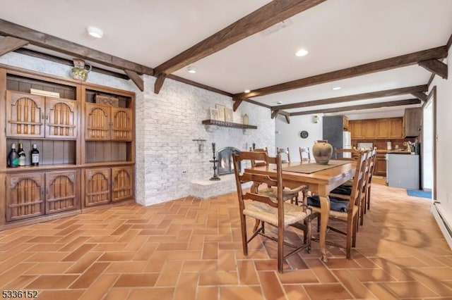 dining space featuring brick wall, a large fireplace, and beam ceiling