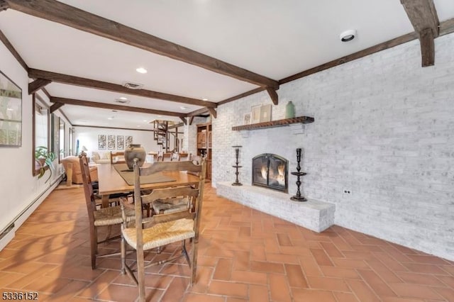 dining room with a brick fireplace, beam ceiling, and brick wall