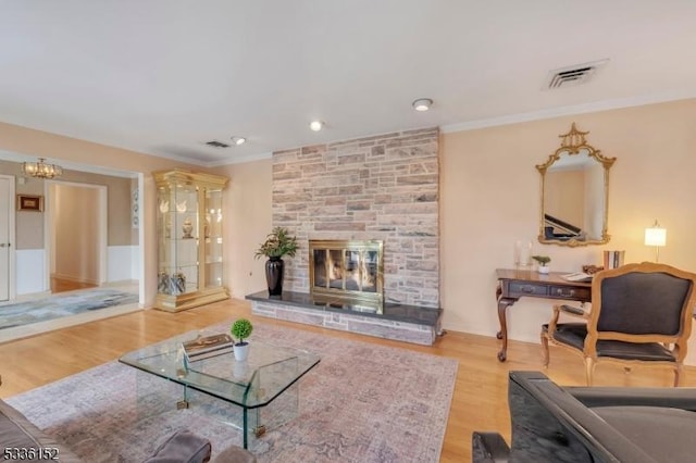 living room featuring crown molding, a stone fireplace, and light hardwood / wood-style flooring