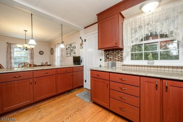 kitchen featuring light wood-type flooring, brown cabinets, light stone counters, backsplash, and hanging light fixtures