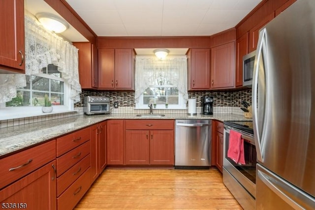 kitchen with a sink, stainless steel appliances, light wood-style floors, and a wealth of natural light