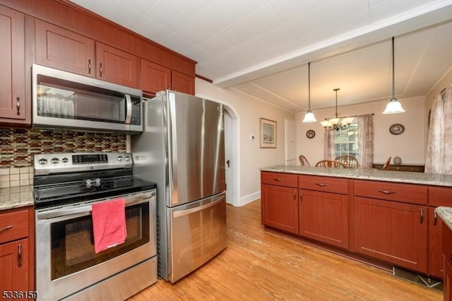 kitchen with light wood-style flooring, arched walkways, appliances with stainless steel finishes, decorative light fixtures, and backsplash