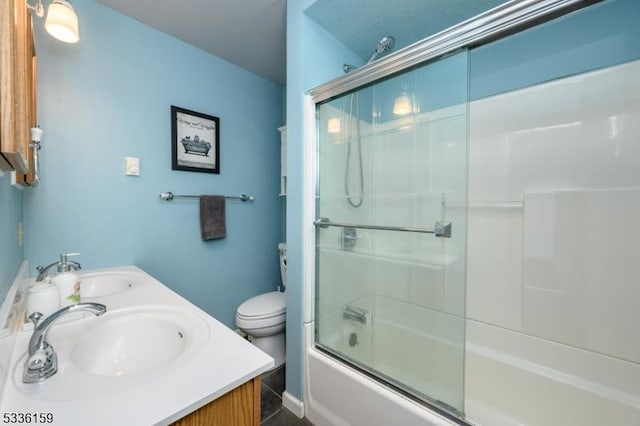 full bath with double vanity, shower / bath combination with glass door, toilet, and a sink