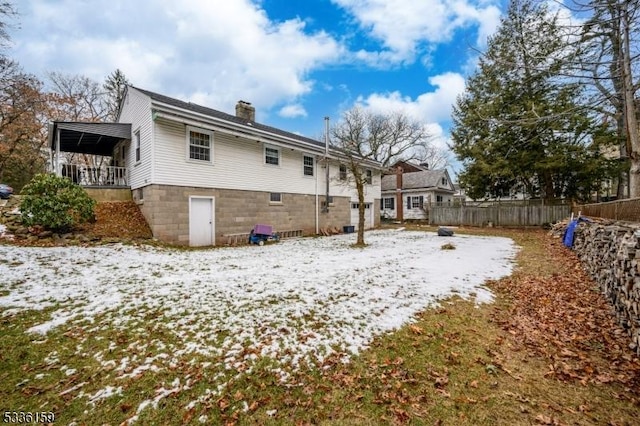 snow covered rear of property featuring a chimney and fence