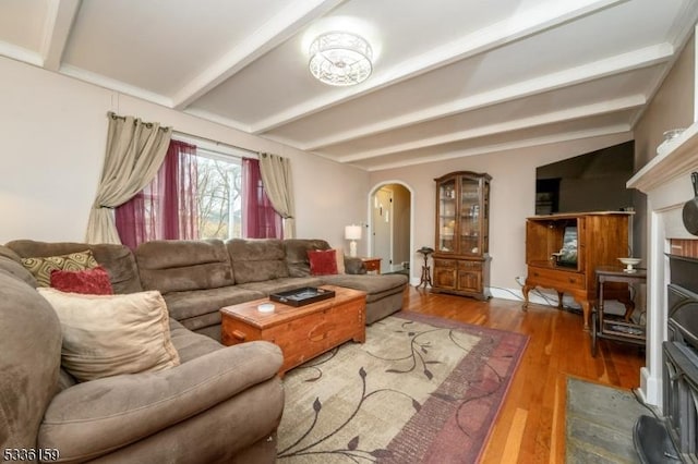 living room featuring beamed ceiling, arched walkways, wood finished floors, and a fireplace with flush hearth